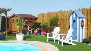 Een achtertuin met een zwembad, een houten schutting, een tuinhuisje en tuinmeubilair.