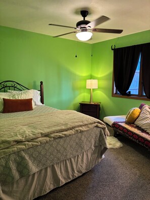 A bedroom with a bed, a nightstand, a lamp, a ceiling fan, and a window with curtains.