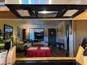 Un espace de vie compact comprenant un coin repas, un téléviseur et une cuisine ouverte sur le reste de la pièce par une porte.