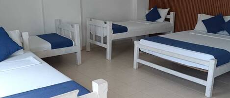 Habitación de hotel con cuatro camas blancas, cada una con ropa de cama azul, cabeceros de madera y un equipo de aire acondicionado en la pared.