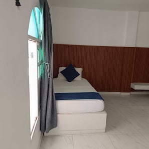 Una cama individual con colchón blanco, manta azul y almohada azul oscuro.