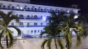 A multi-story building with balconies, palm trees in the foreground, and a pool area.