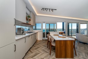 A modern kitchen with a herringbone floor, a dining area with a wooden table, and large windows offering a view. - Modern Sea View Penthouse with Private Terrace – 20 Min to IST (Karaburun)