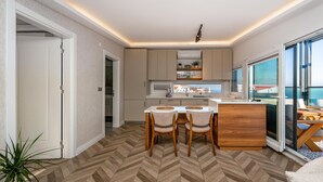 A modern kitchen with a herringbone floor, a dining area with two chairs, and a view of the sea through large windows. - Modern Sea View Penthouse with Private Terrace – 20 Min to IST (Karaburun)