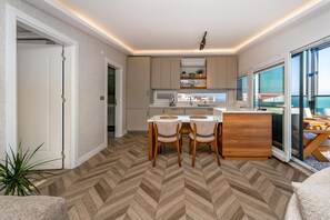 A modern kitchen with a herringbone floor, a dining area with two chairs, and a view of the sea through large windows. - Modern Sea View Penthouse with Private Terrace – 20 Min to IST (Karaburun)