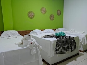 Habitación de hotel con dos camas, cada una con ropa blanca y una manta color turquesa.