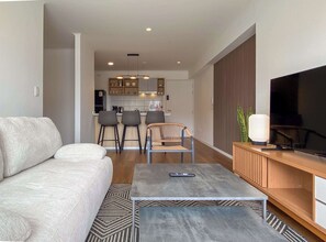 A modern living room with a sofa, a coffee table, a TV, and a kitchen in the background. - w* | Upscale 2BR w/ Balcony & View in Miraflores (Miraflores)