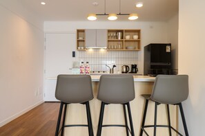 Een moderne keuken met drie barkrukken, een zwarte koelkast en een houten plank met servies.