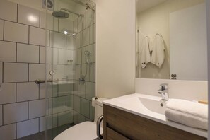Een moderne badkamer met een douchecabine van glas, een witte wastafel en een houten meubel.