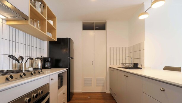 Una cocina moderna con armarios blancos, estufa integrada y refrigerador negro.