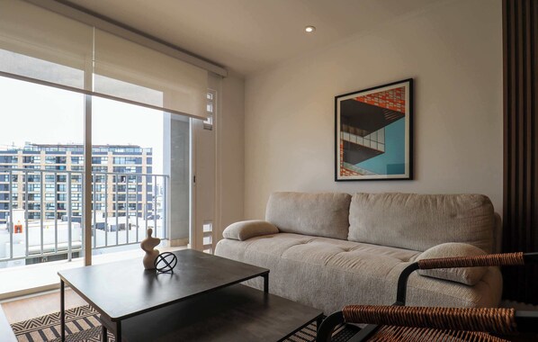 Een moderne woonkamer met een bank, een salontafel en een stoel. Er is een groot raam met uitzicht op gebouwen.