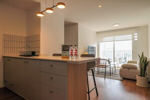 A modern kitchen with a large island, a dining area with a view, and a living space with a plant. - w* | Stylish 2BR w/ Balcony & View in Miraflores (Miraflores)