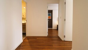 Un pasillo con suelo de madera, paredes blancas y puertas abiertas que dan a otras habitaciones.