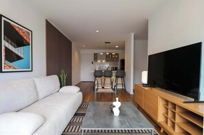 Een moderne woonkamer met een bank, een salontafel, een televisie en een eethoek op de achtergrond.