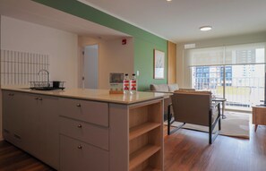 A modern kitchen with a central island, a dining area with a sofa and table, and a large window offering a view of the city. - w* | Curated Urban 2BR w/ Balcony in Miraflores (Miraflores)