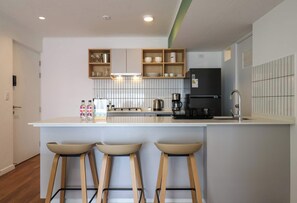 A modern kitchen with a central island, bar stools, a coffee machine, and a black refrigerator. - w* | Curated Urban 2BR w/ Balcony in Miraflores (Miraflores)