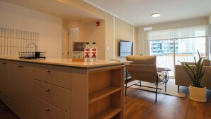 A modern hotel room with a kitchenette, a seating area with a sofa and armchairs, a large window with a view, and a flat-screen TV mounted on the wall. - w* | Light-Filled 2BR w/ Balcony in Miraflores (Miraflores)