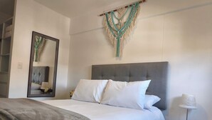 Un letto rifatto con lenzuola bianche, una testiera grigia e un comodino con una lampada.