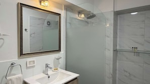 Ein modernes Badezimmer mit einem großen Spiegel, einem Waschbecken, einer Duschkabine aus Glas und Marmorfliesen.