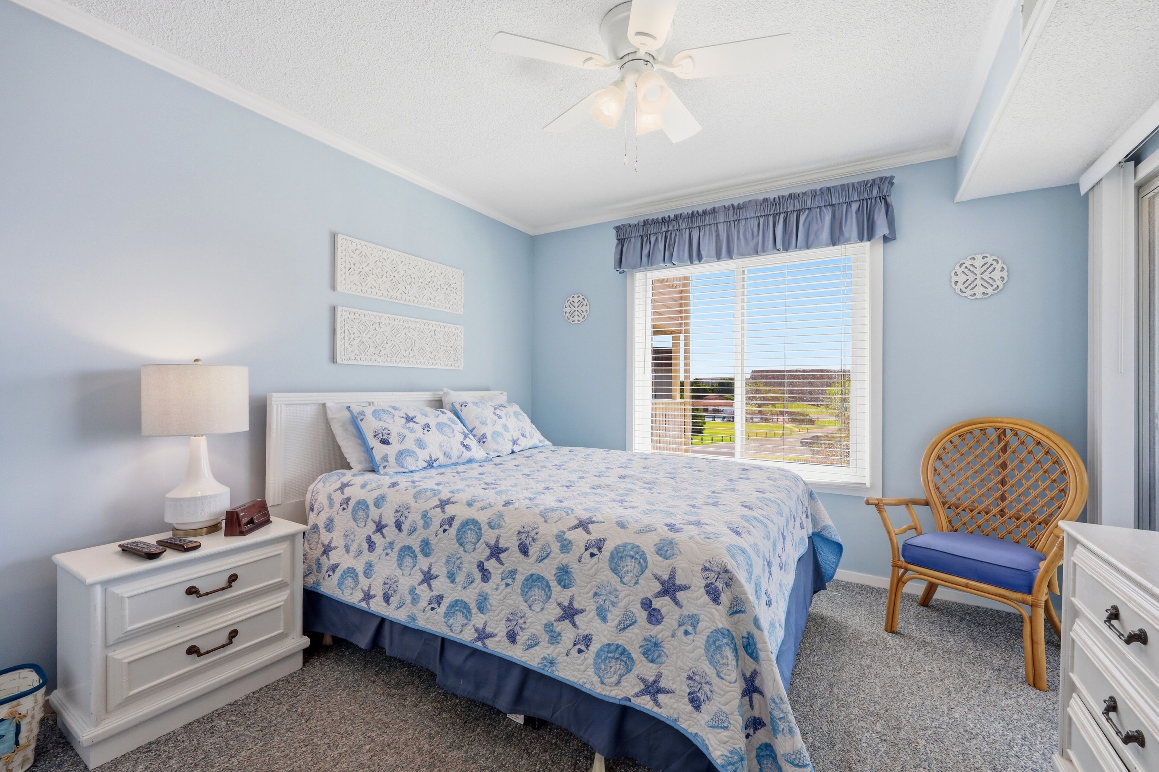 Une chambre à coucher comprenant un lit, une table de chevet, une chaise, une commode et une fenêtre avec des stores.