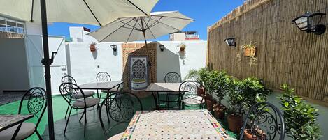 An outdoor patio with tables and chairs, a large umbrella, potted plants, and a decorative wall.