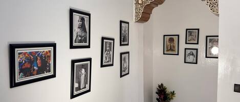 Um corredor com quadros nas paredes, um vaso de planta e um arco decorativo.