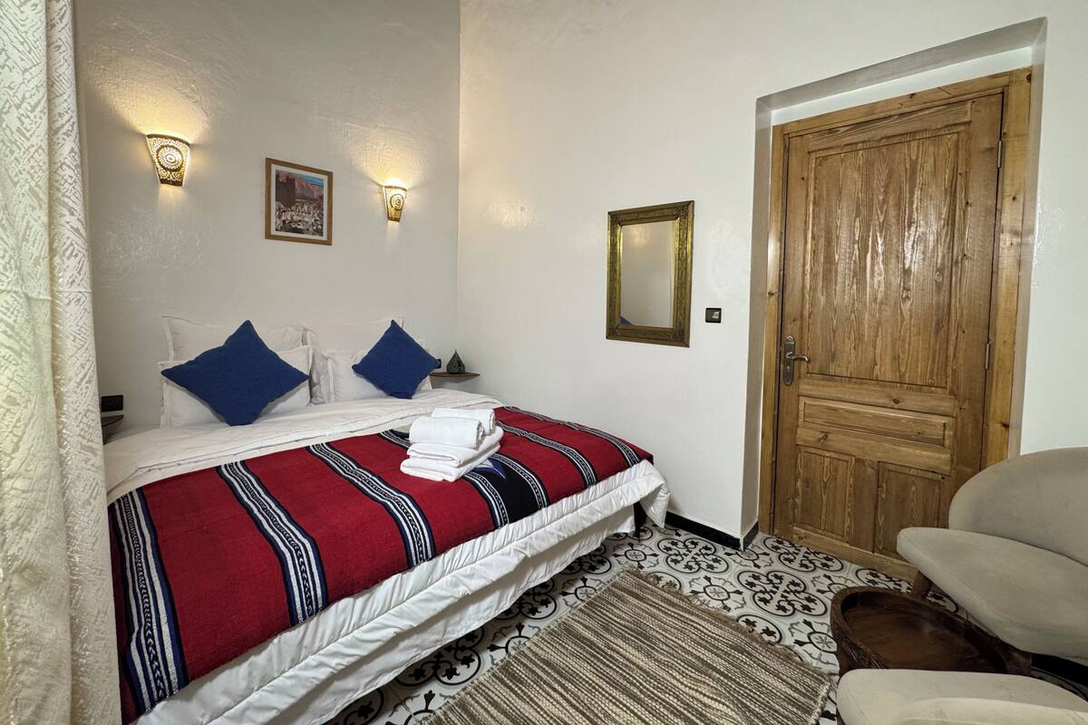 A hotel room with a bed, a wooden door, a chair, and a patterned rug.