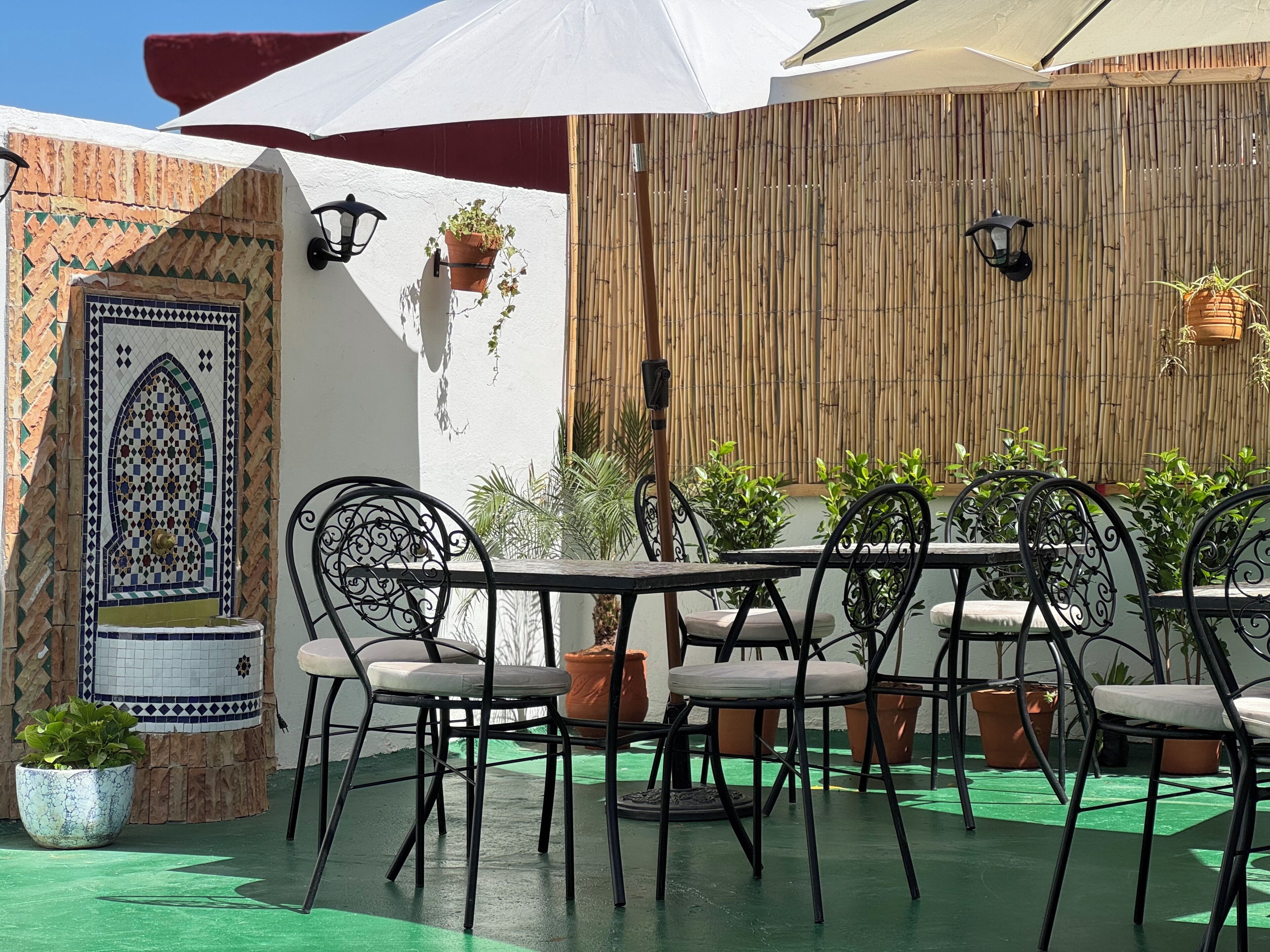 An outdoor patio with a table and chairs, potted plants, a decorative door, and a bamboo wall.