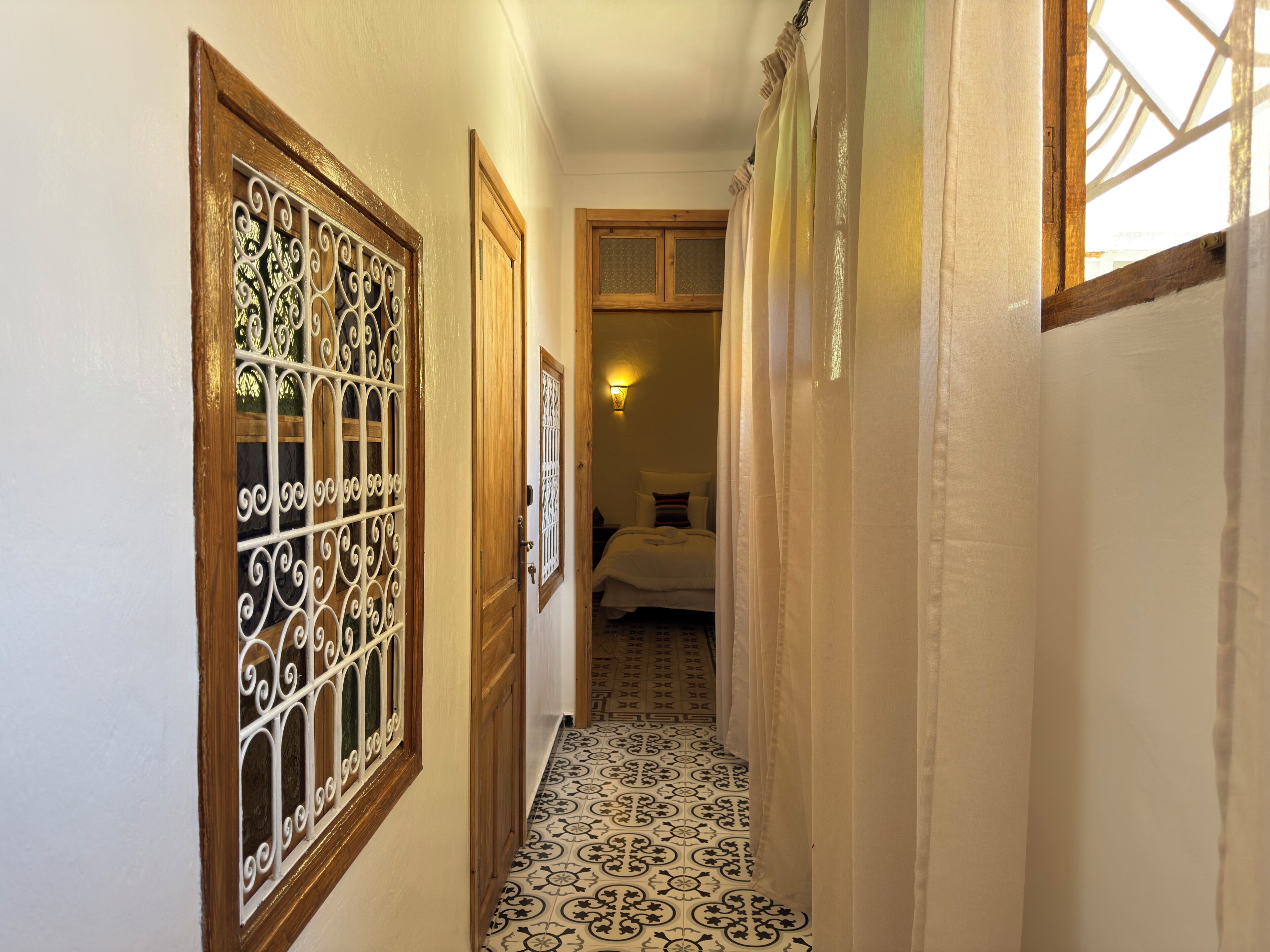 Un pasillo estrecho con baldosas de suelo estampadas, puertas de madera y una cama al fondo.