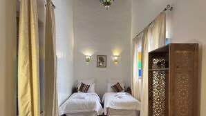 Una habitación con dos camas, un armario de madera, un tapete estampado y un panel decorativo en la pared.