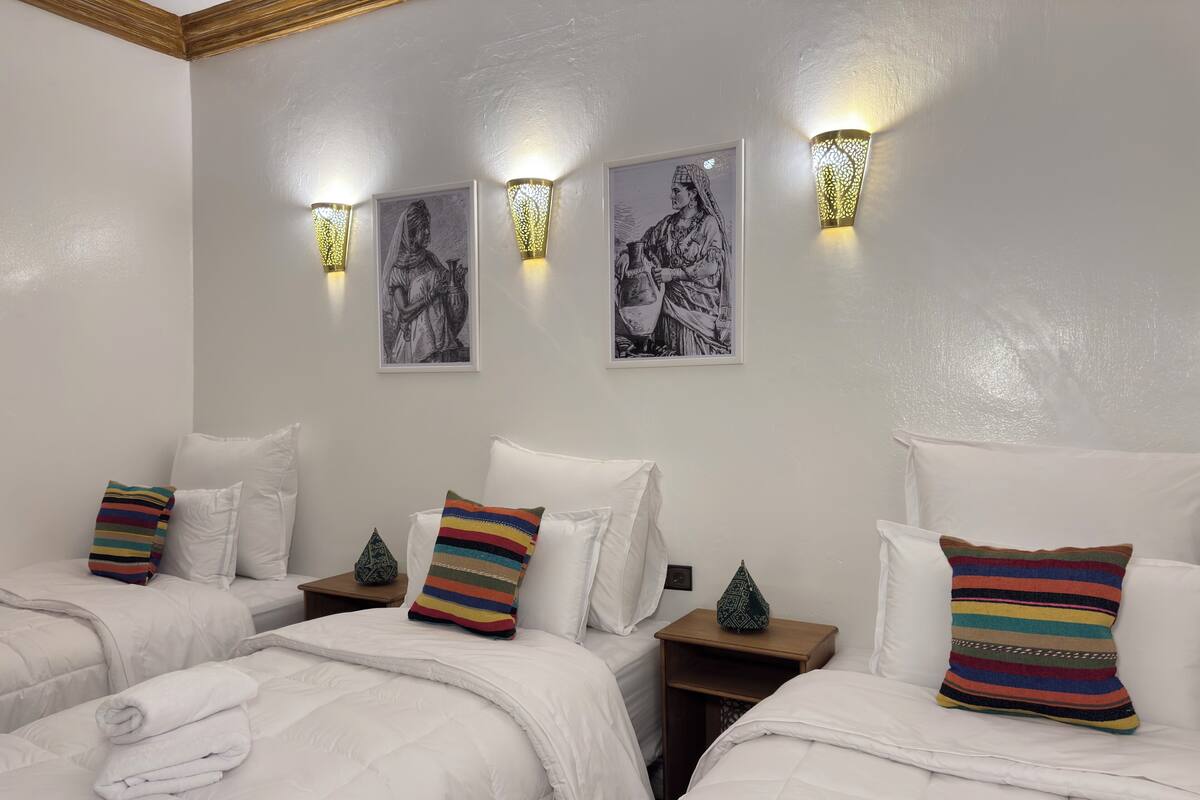 A hotel room with two beds, white bedding, striped pillows, wall-mounted artwork, and decorative wall sconces.