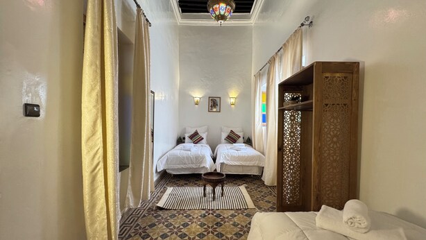 Habitación de hotel con dos camas, piso estampado, puerta de madera decorativa y candelabro.