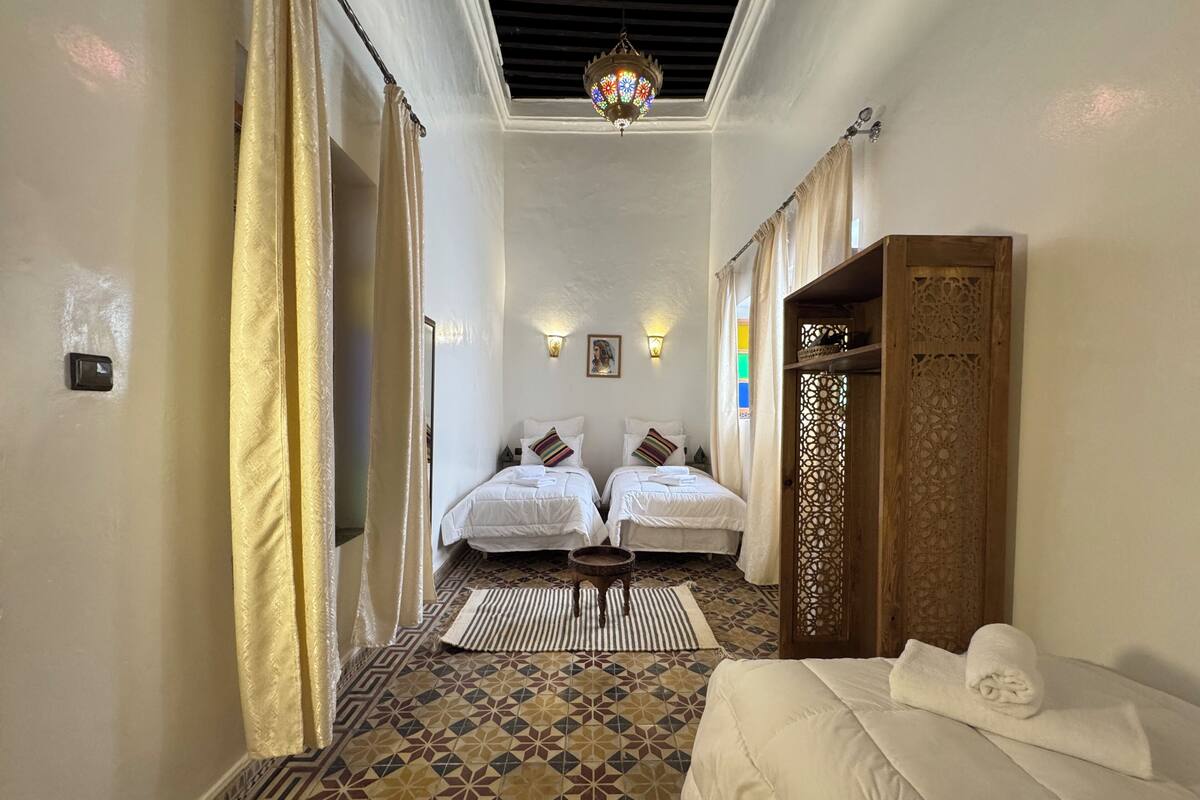 A hotel room with two beds, a patterned floor, a decorative wooden door, and a chandelier.