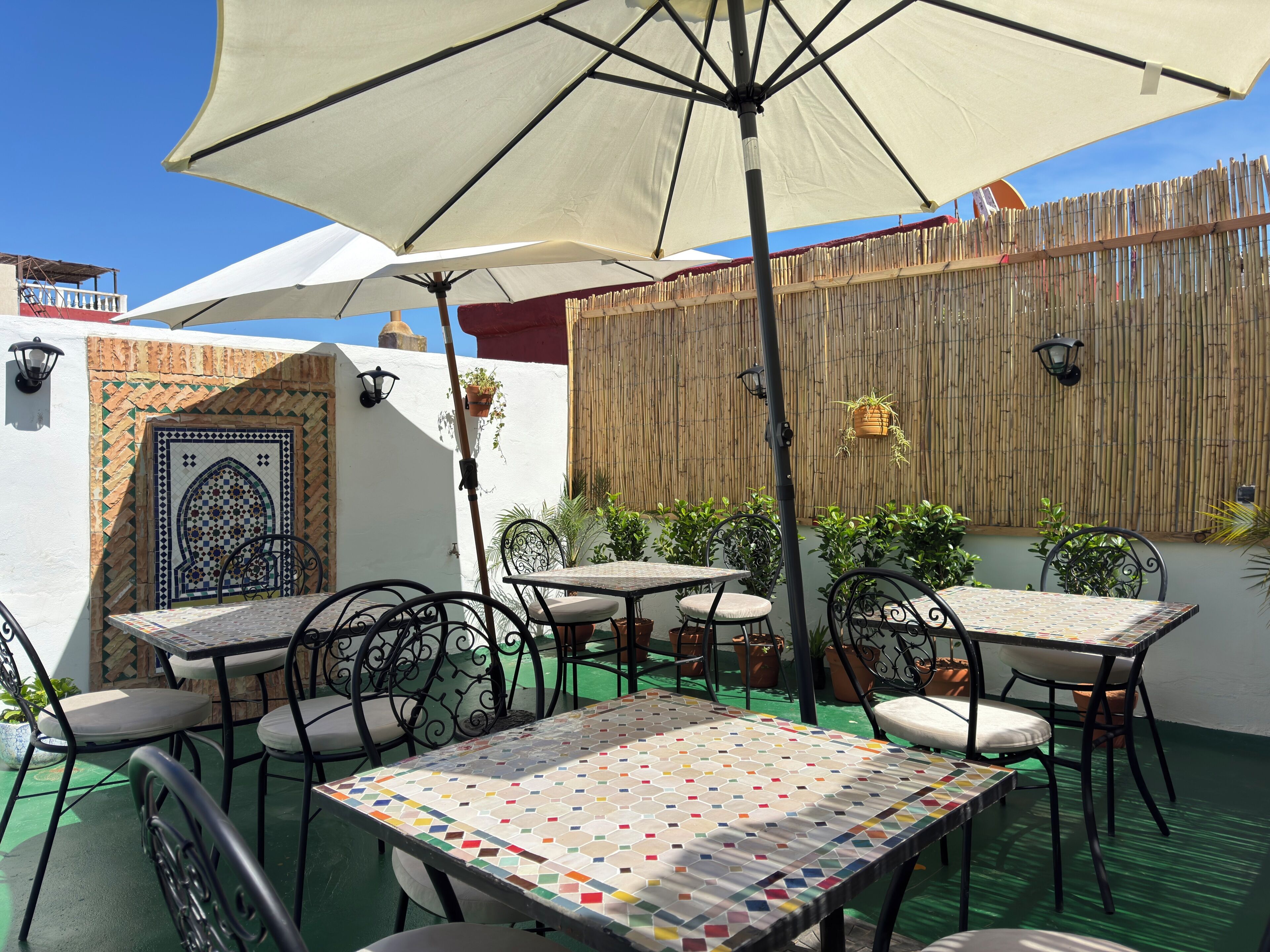 Un espace extérieur aménagé en terrasse, avec des tables et des chaises, un grand parasol et un mur décoratif.