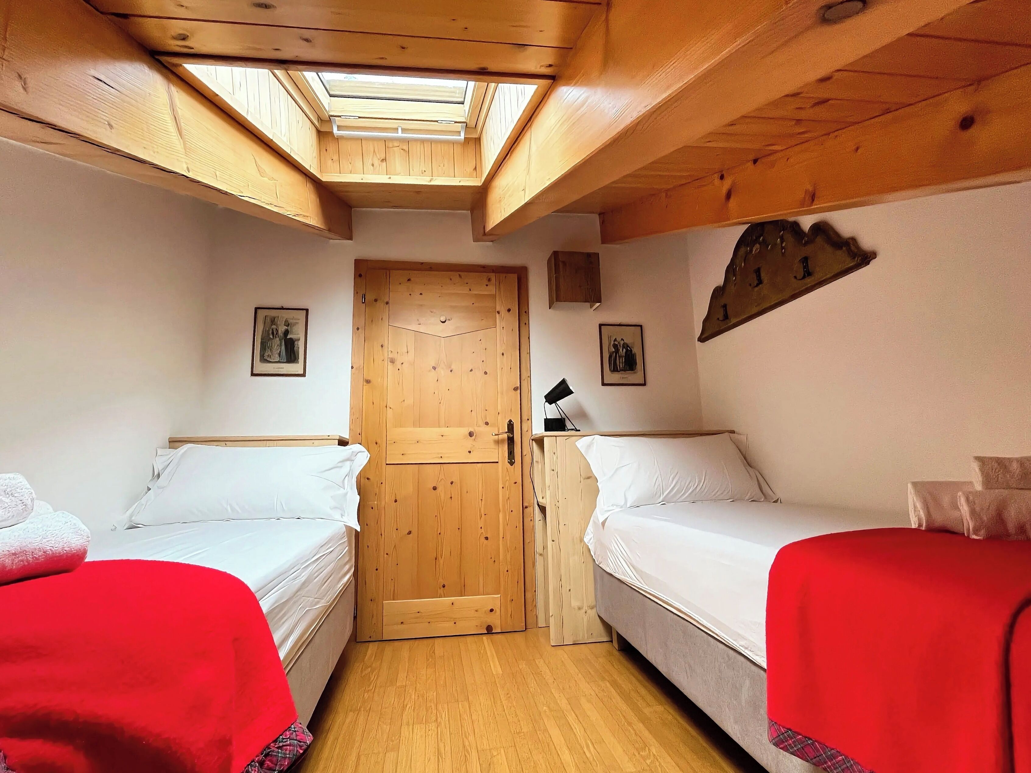 A bedroom with two beds, a skylight, wooden ceiling beams, and a door.