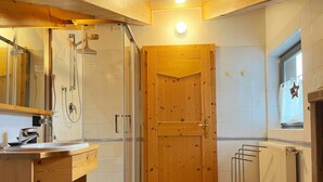 Ein Badezimmer mit Duschkabine, Holztür, weißer Toilette und Waschbecken mit Spiegel darüber.