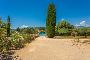 A gravel path leading to a blue gate, surrounded by greenery and trees. - Le Mas Valou, stone villa with pool (Tourrettes)