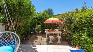 Une terrasse avec un fauteuil suspendu, une table avec quatre chaises et un parasol coloré.
