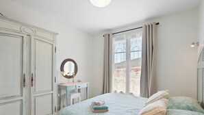 Une chambre à coucher comprenant un lit, une commode, un bureau, une fenêtre avec des rideaux et une vue sur l’extérieur.