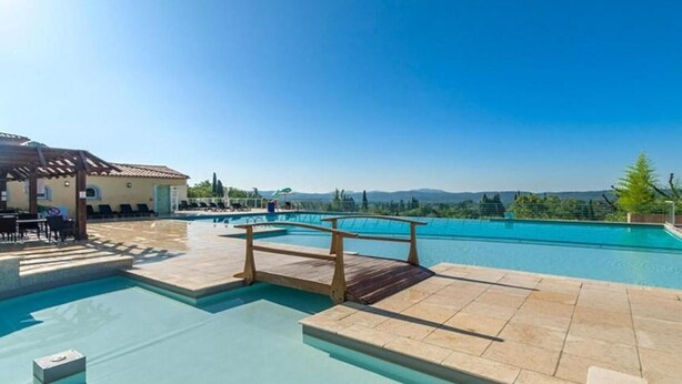 Une piscine avec une terrasse en bois, un espace salon couvert et une vue sur les montagnes.