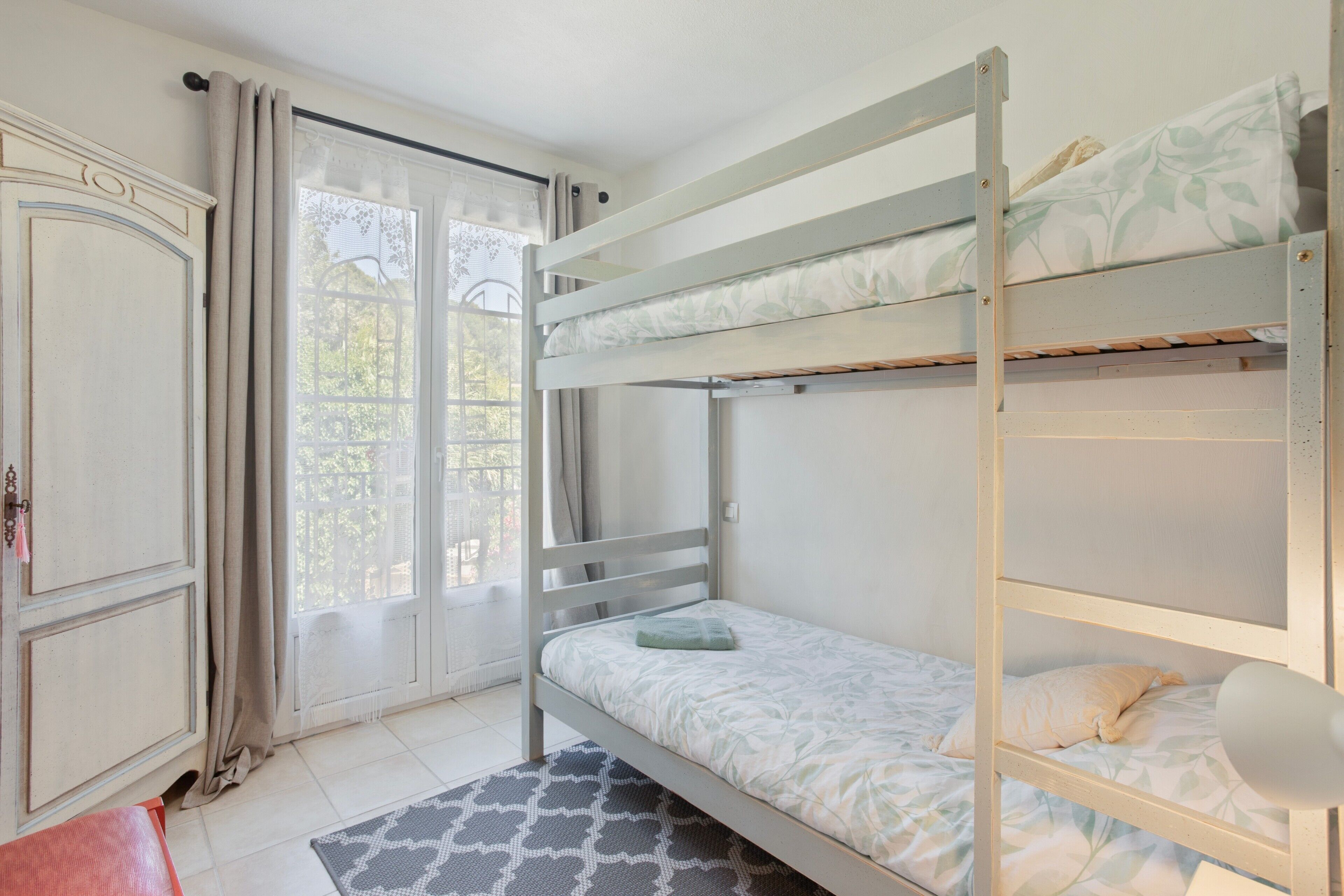 Une chambre avec un lit superposé, une fenêtre, des rideaux et un tapis à motifs.