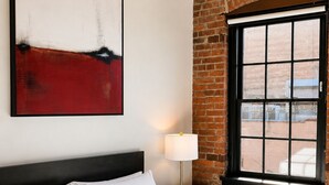 Ein Hotelzimmer mit Bett, Fenster mit Blick, einer Lampe und einem Gemälde an der Wand.