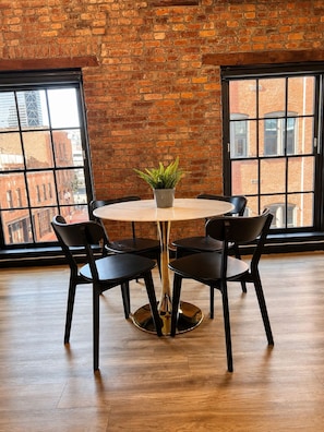 A round table with four chairs, a potted plant, and a brick wall with large windows. - Brick & Bed - Riverfront Loft - Convention Center (St. Louis)