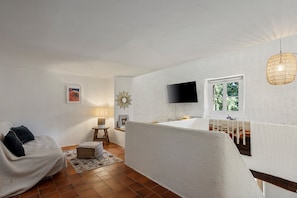 Une pièce comprenant un canapé, une petite table avec une lampe, un téléviseur fixé au mur et une fenêtre donnant sur un paysage verdoyant.