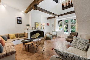 Tilava olohuone, jossa on takka, sohvaryhmä, ruokapöytä ja useita erilaisia tuoleja.