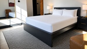 Una habitación de hotel moderna con una cama grande, mesitas de noche, un espejo, una silla y una alfombra estampada.