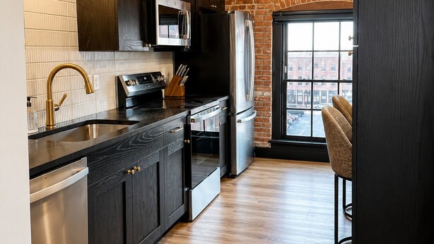 Una cocina moderna con armarios de madera oscura, electrodomésticos de acero inoxidable, una pared de ladrillo y un ventanal grande.