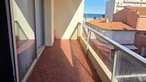 Een balkon met betegelde vloer, een glazen deur en uitzicht op gebouwen en de zee.