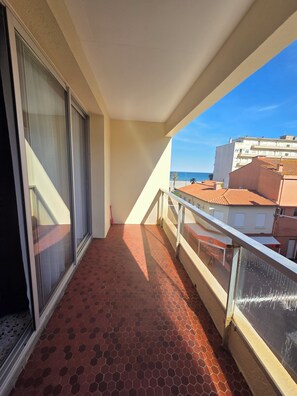 Ein Balkon mit Fliesenboden, einer Glastür und Blick auf Gebäude und das Meer.
