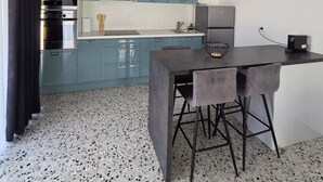 Een moderne keuken met blauwe kastjes, een zwarte afzuigkap en een eethoek met een tafel en stoelen.